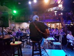Pub with dancing at Die Watergat with people listerning to an artist playing and singing on a stage inside this venue.
