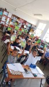 Learners smile and raise their hands in a classroom in Langebaan Primary School