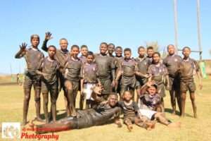 School rugby team pose for a photo after a match, covered in mud in Langebaan