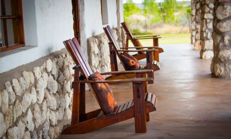 Love weskus ilove weskus ithe patio of the farmhouse at thali thali game lodge showing the traditional patio with 3 wooden chairs and stone finishing to the exterior wall of the building.
