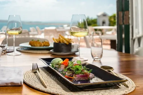 Iiseafood on a plate at a restaurant with langebaan lagoon in the back drop. Table has plate, cutlery, wine in a glass and chips all at fine dining in langebaan. Enjoy seafood in style