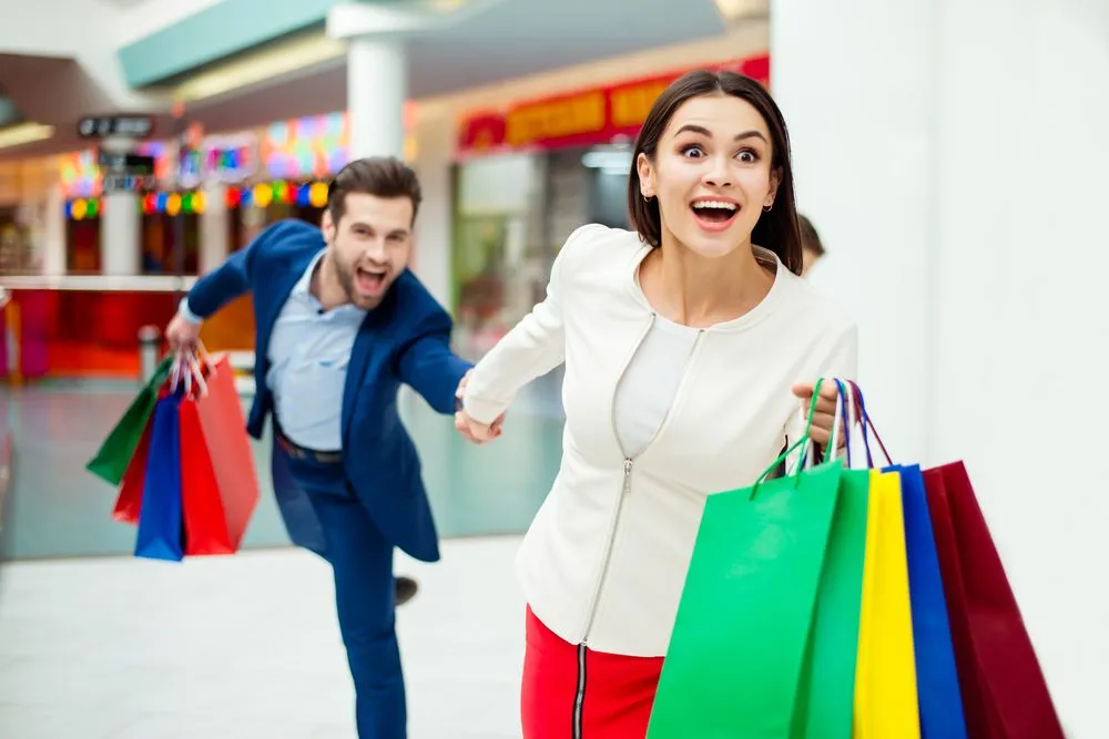 Iihave fun shopping in langebaan. Wife running through mall dragging husband behind, holding onto shopping bags