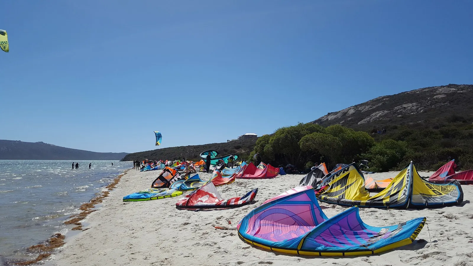 Iithe beach at shark bay in langebaan with different kitesurfing sails on the beach. Flat waters and people in the distance.