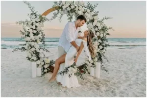 Iia couple with their wedding on the beach in langebaan. They are surrounded with a circle of flowers , holding each other on the beach.
