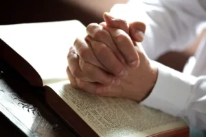 Love weskus ilove weskus ia person sits with hands crossed on top of an open bible in a pray position at a place of worship in langebaan