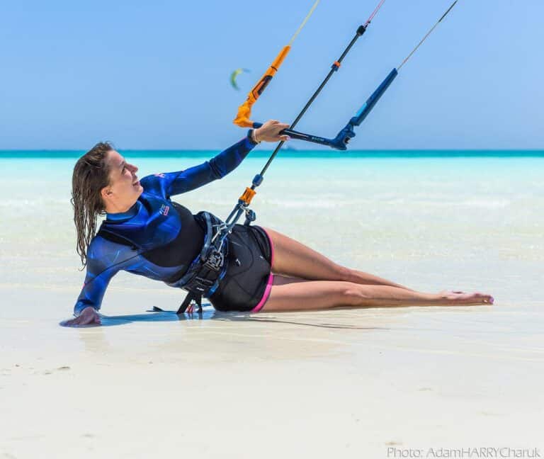 Iia lady lies on the beach and with one hand tries to control her kite in the wind as she learns kite surfing in langebaan