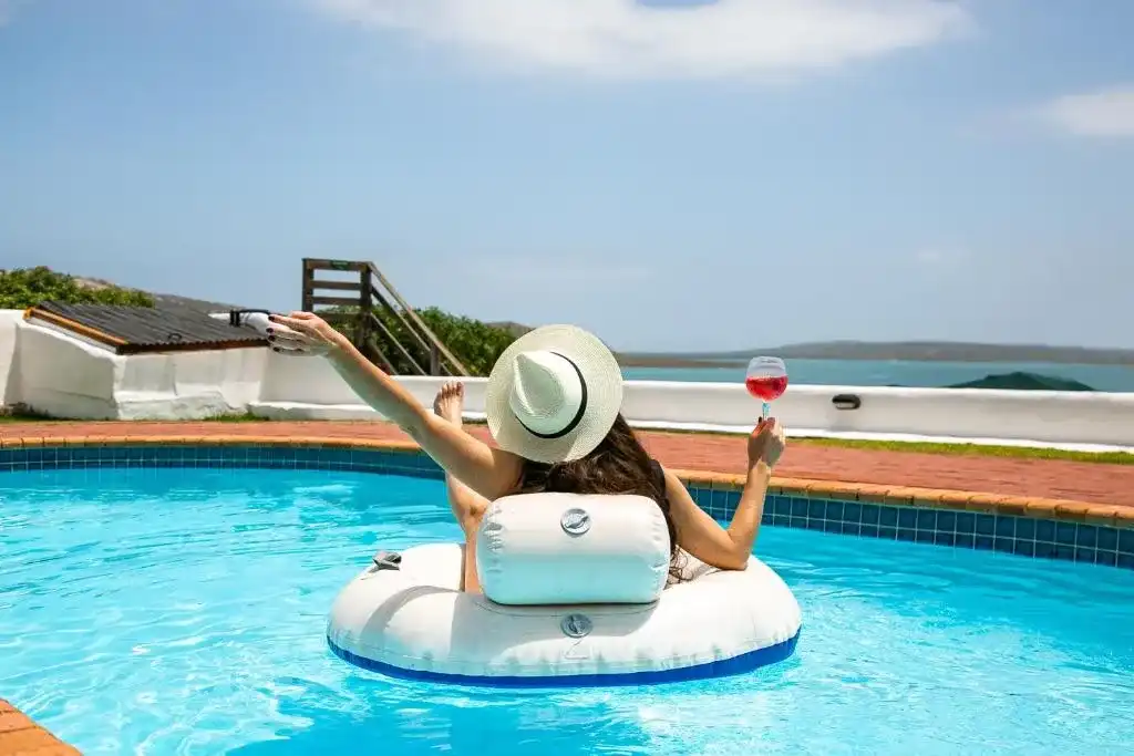 Iigirl relaxes in a swimming pool with a cocktail enjoying the view over the langebaan lagoon after finding langebaan accommodation for a great staycation. Variety options available for all budgets.