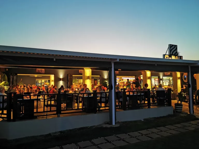 Iilots of people sitting at sunset on the deck of kokomos restaurant in langebaan with lights on creating a nice setting.