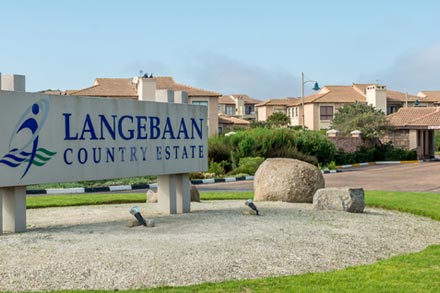 Love weskus ilove weskus ian entrance sign for the langebaan country estate in blue letters on a board with houses in the back ground.