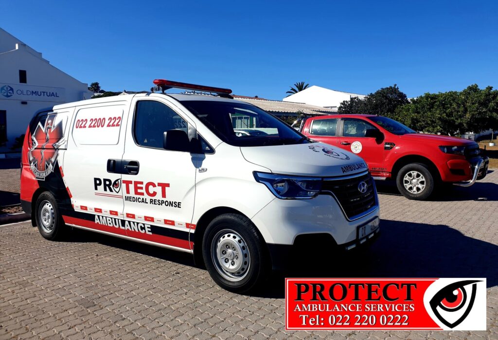 White PROTECT Medical Response ambulance with red stripe and a red emergency light on top, parked beside a red pickup truck; large red PROTECT sign with phone number in the foreground; Old Mutual building in the background under a clear blue sky.