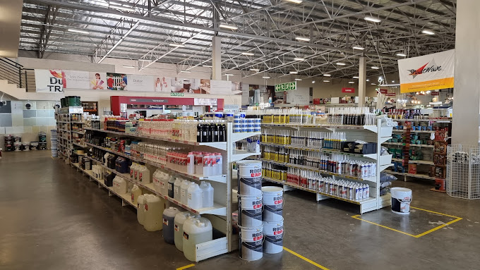 Wide view of a warehouse-style home improvement store with tall metal shelves stocked with paint, containers, and cleaning supplies along an aisle.