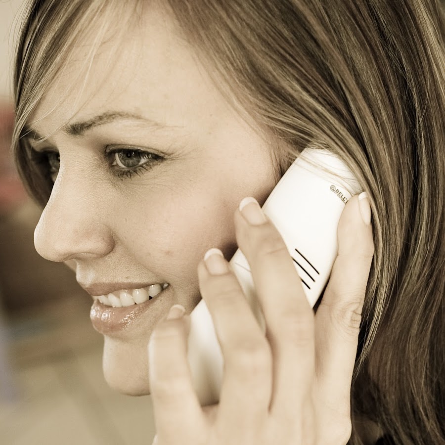 Close-up of a woman smiling while talking on a white mobile phone held to her ear, in profile view.