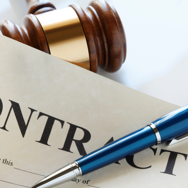 Close-up of a wooden gavel resting on a parchment contract with a blue pen nearby, suggesting legal paperwork and signing.