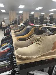 Row of casual leather boots on a display table inside a shoe store, with more shoes arranged on racks in the background.