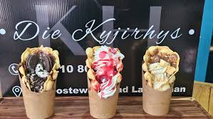 Three ice cream cones with varied toppings on a wooden counter in front of a shop sign.