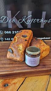 Two slices of orange loaf with raisins on a wooden board, placed beside a small jar of jam.