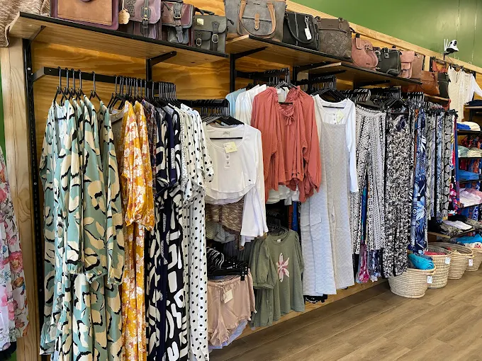 Clothing rack in a boutique with patterned dresses and tops, handbags on the shelf above.