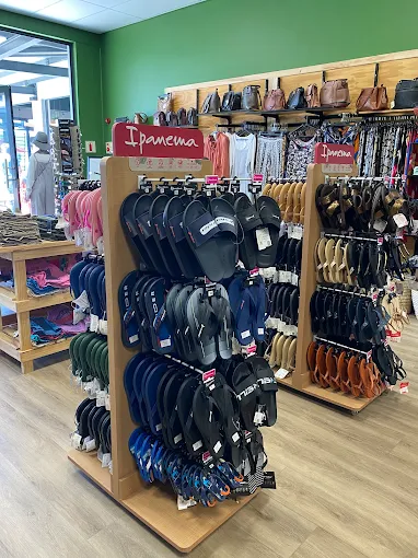 Shoe store display with wooden racks of flip-flops organized by color; green walls and a bright overhead light, Ipanema-branded signs visible on the racks.