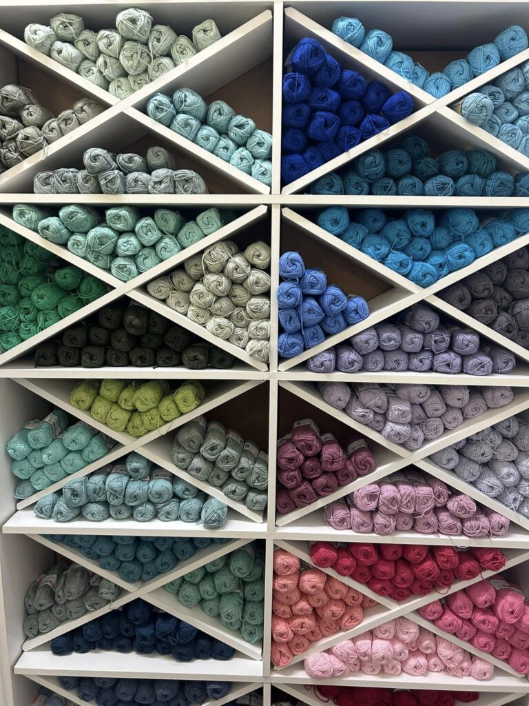 Shelves filled with pastel to bright yarn skeins arranged by color, in a diamond grid display.