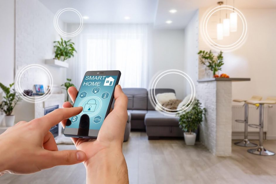 Hand holding a smartphone showing a smart home app while lounging in a bright living room.