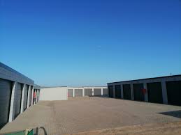 Row of storage unit garages with closed doors along a paved courtyard under a clear blue sky.