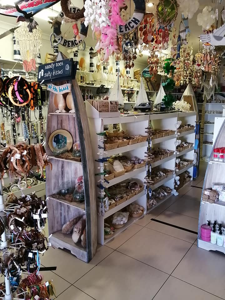 Store interior filled with beach-themed souvenirs, shells, and jewelry on shelves in a bright shop
