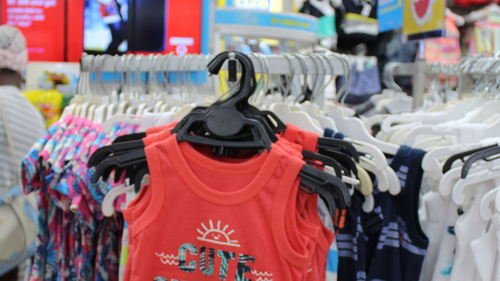 Red sleeveless children's shirt with sun graphic and the word 'CUTE' on a hanger in a store display.
