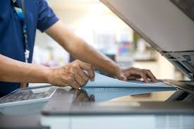 Person in a blue shirt uses the touchscreen on a large office copier/scanner to scan a document let on the glass surface.