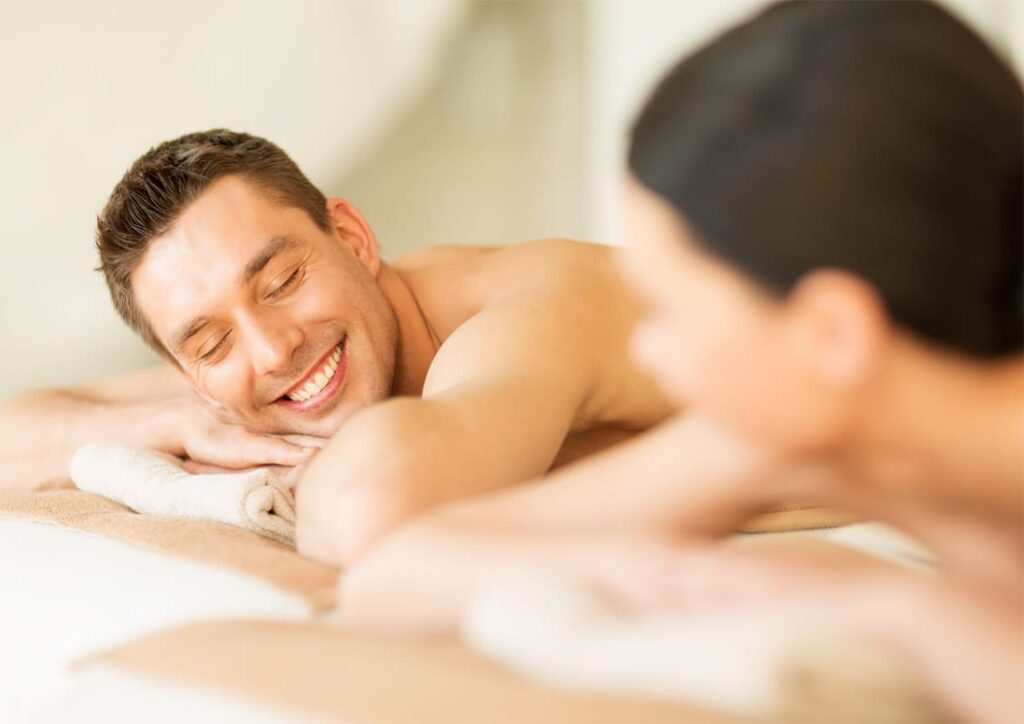 Man smiling with eyes closed, resting his head on a towel during a massage at a spa.