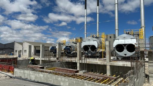Construction site with large cylindrical industrial units, scaffolding, and a worker in a hard hat under a blue sky