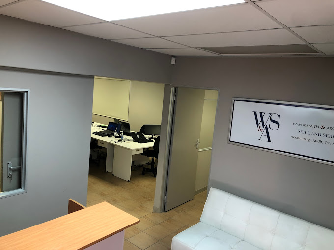 Professional office reception with a white sofa, wooden desk, and open-workspace doorway; wall sign 'WSA'.