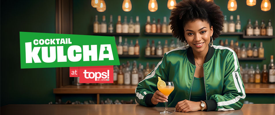Woman in a green jacket at a bar, holding an orange cocktail, beside a 'Cocktail Kulcha at Tops' banner.