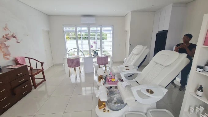 Face boutique – – Iibright, modern spa with three white pedicure chairs, a manicure station by large windows, purple accent chairs, and a staff member near shelves on the right.