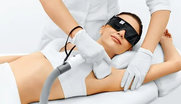 Hair-removal-services-langebaan-1 webp – – Iiwoman undergoing cosmetic laser hair removal; wearing protective goggles while a clinician in gloves operates the handheld device on her underarm area.