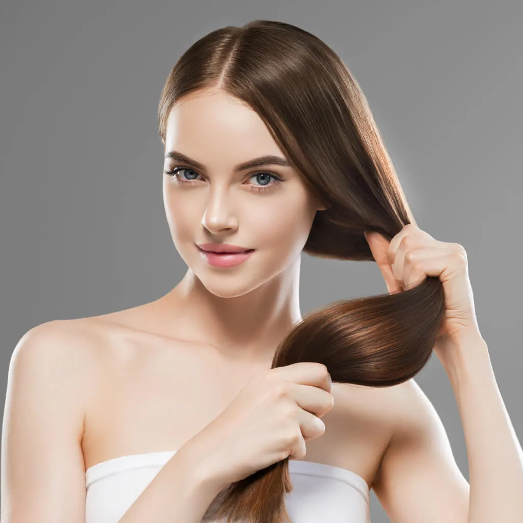 Hair-treatments-langebaan – – Iiportrait of a young woman with long glossy brown hair, holding a strand to show its shine and smoothness.