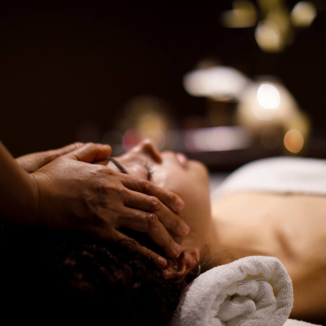 Lbn boutique hotel spa langebaan – – Iitherapist's hands massage a client's scalp during a spa treatment, client lying with a towel wrapped around the head in dim lighting.
