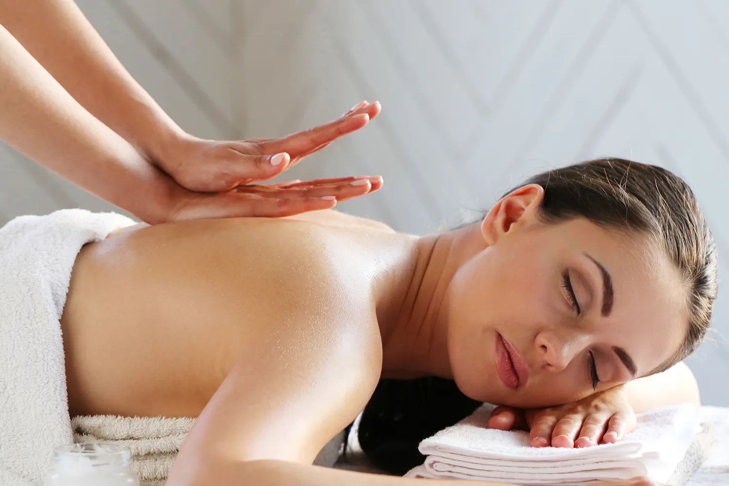 Iiwoman lying on a massage table with eyes closed as a therapist massages her back.